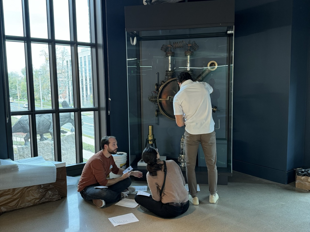 Three people in a museum gallery, two are seated.